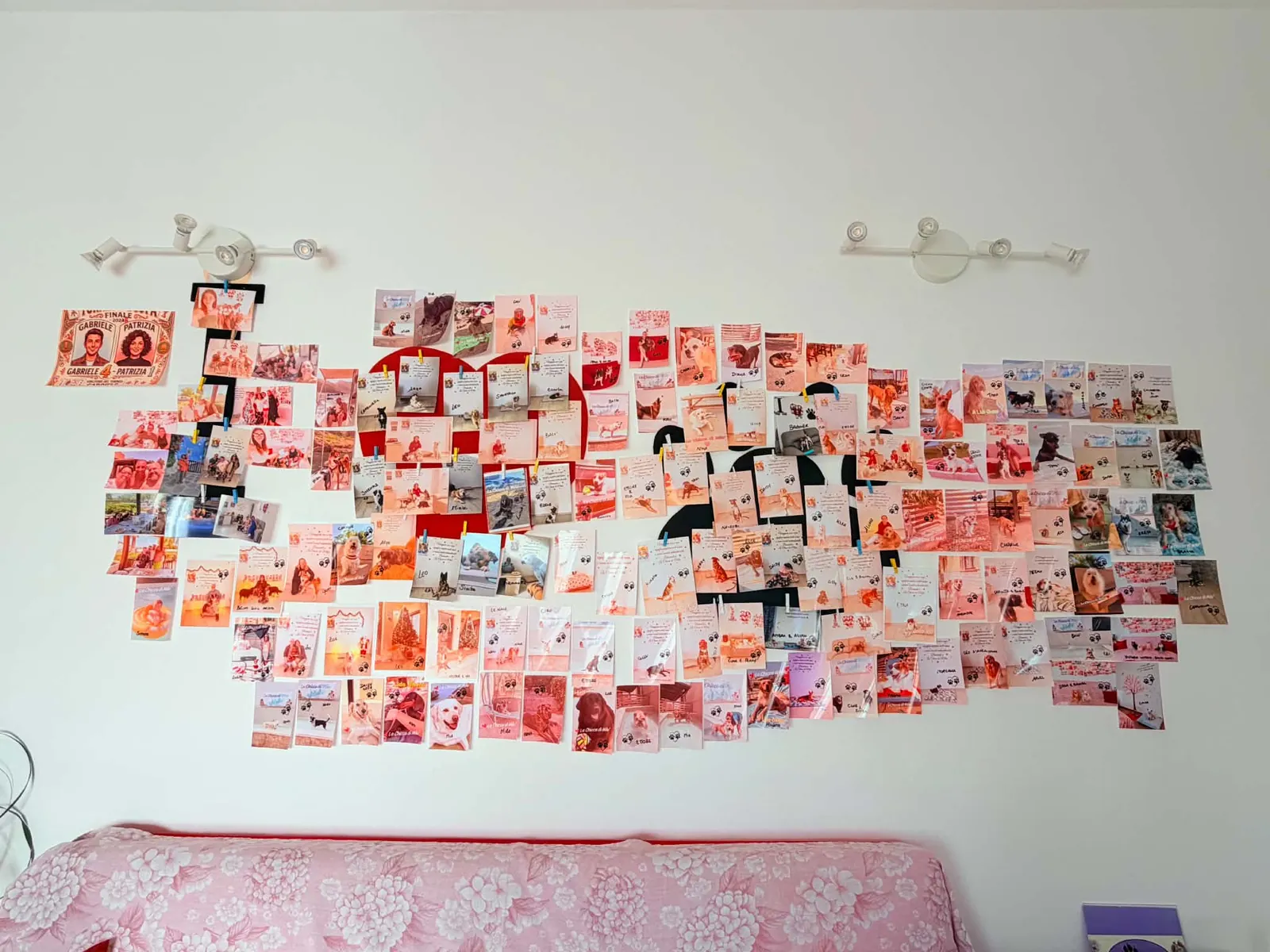 Una parete bianca coperta da decine di foto ricordo degli ospiti a quattro zampe, stampate e appese una accanto all'altra fino a formare un grande mosaico, sopra un letto con copriletto rosa.